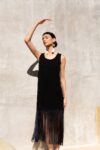 Model wearing the Ceiba fringe dress in black, featuring a minimalist silhouette with long flowing fringe. Styled with Maya earrings under natural sunlight