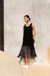 Model wearing Naay Earrings with bull horn and natural fiber fringe, styled with a black dress against a sunlit wall.