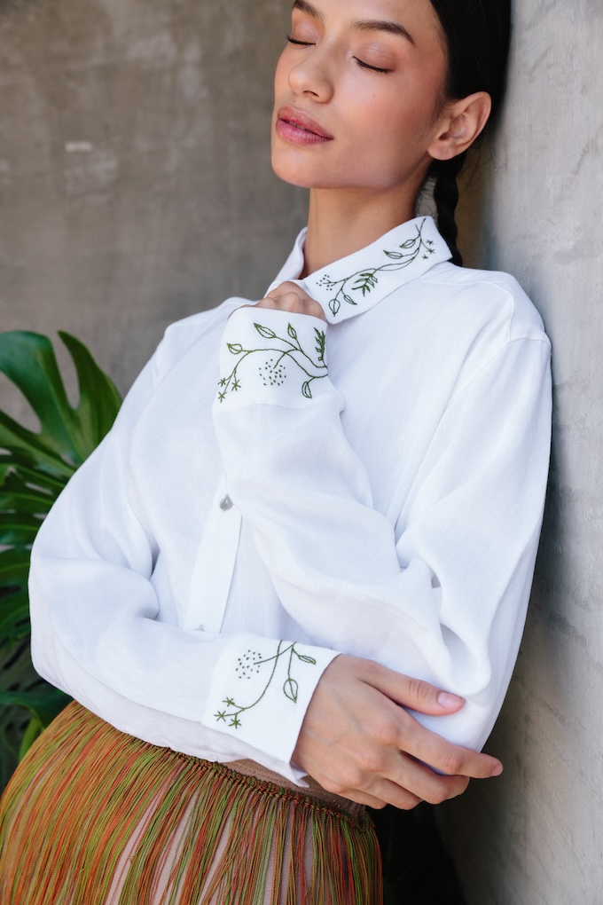 Model wears Hiedra embroidered linen shirt in white Italian linen, detailed with green hand embroidery by Temoaya artisans