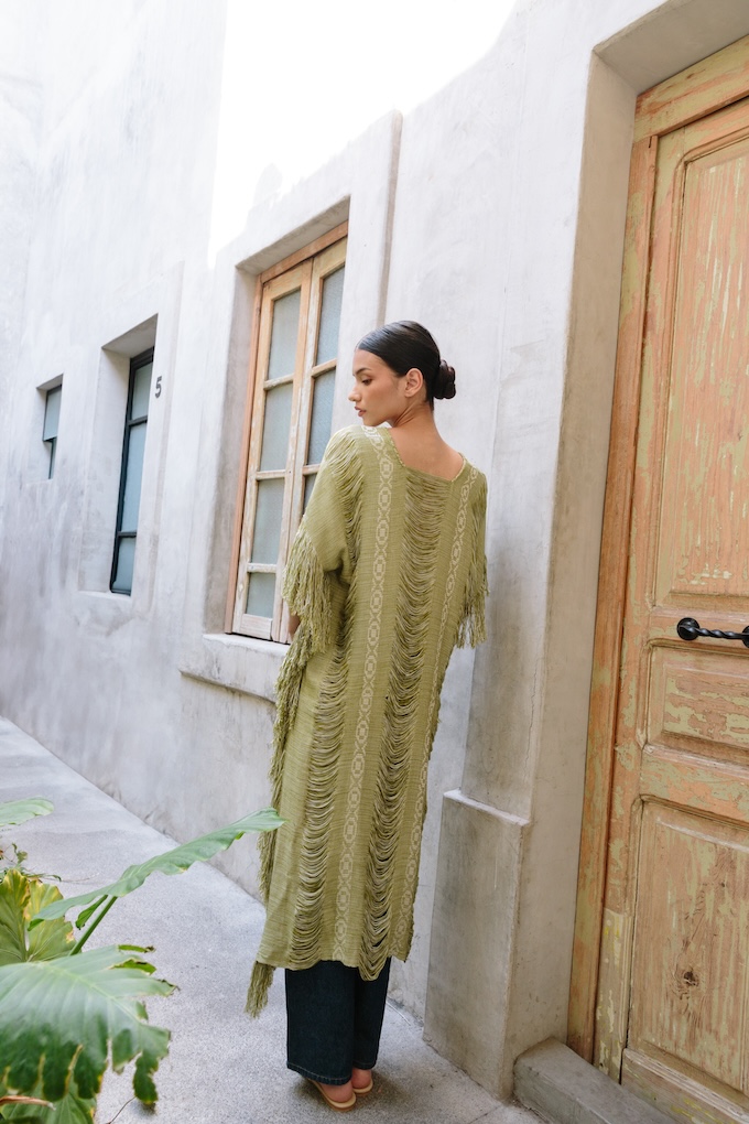 Back view of the Xpu-Ha Kimono showing its handwoven fringe and elongated silhouette, styled with relaxed jeans and minimal footwear.